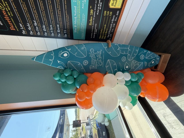Orange, teal and white organic balloon garland by a restaurant surfboard sign