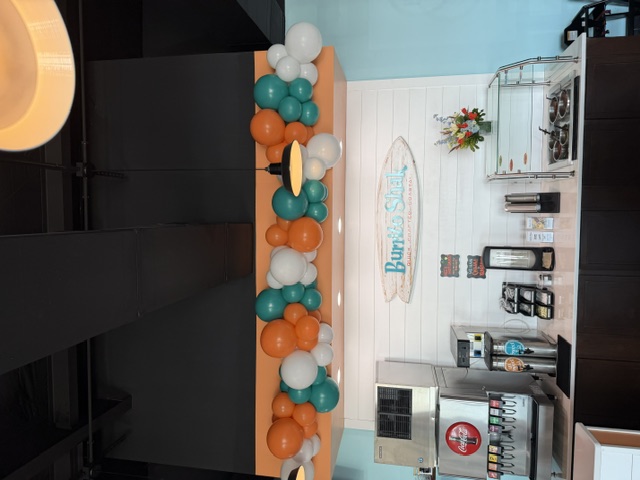 Orange and teal balloon garland installed above a café beverage counter